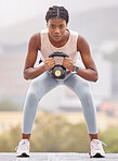 Fitness, squat and black woman with weight in the city, exercise energy and training for health on a rooftop in Turkey. Wellness, strength training and portrait of a girl with a kettlebell for muscle
