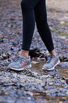 Woman, running shoes and feet in mud while hiking in nature for fitness, exercise and cardio training outdoor for health, travel and wellness on adventure. Legs of female athlete walking forest path