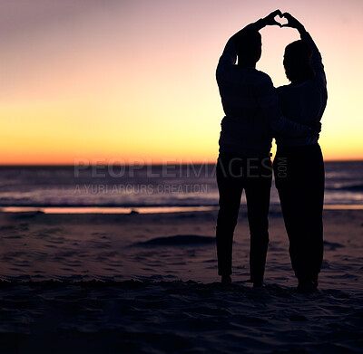 Buy stock photo Couple, sunset silhouette and beach with heart sign hands, bonding and love on vacation for honeymoon. Man, woman and romantic hand signal by ocean with dusk sunshine for romance together in nature