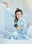 Headphones, phone and woman in bed dancing while listening to music, playlist or radio at her home. Happy, smile and young lady from Canada in pajamas streaming audio, album or song with a cellphone.