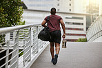 Fitness, city or black man walking to gym on a bridge with a sports bag or water bottle for a workout or exercise. Back view, motivation or healthy person traveling to a training center or club