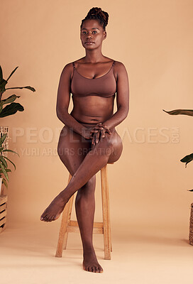 Buy stock photo Black woman, body and beauty while in underwear on a chair against a peach background for cosmetics, body positivity and self love with cosmetics. Dark skin girl portrait for skincare and wellness
