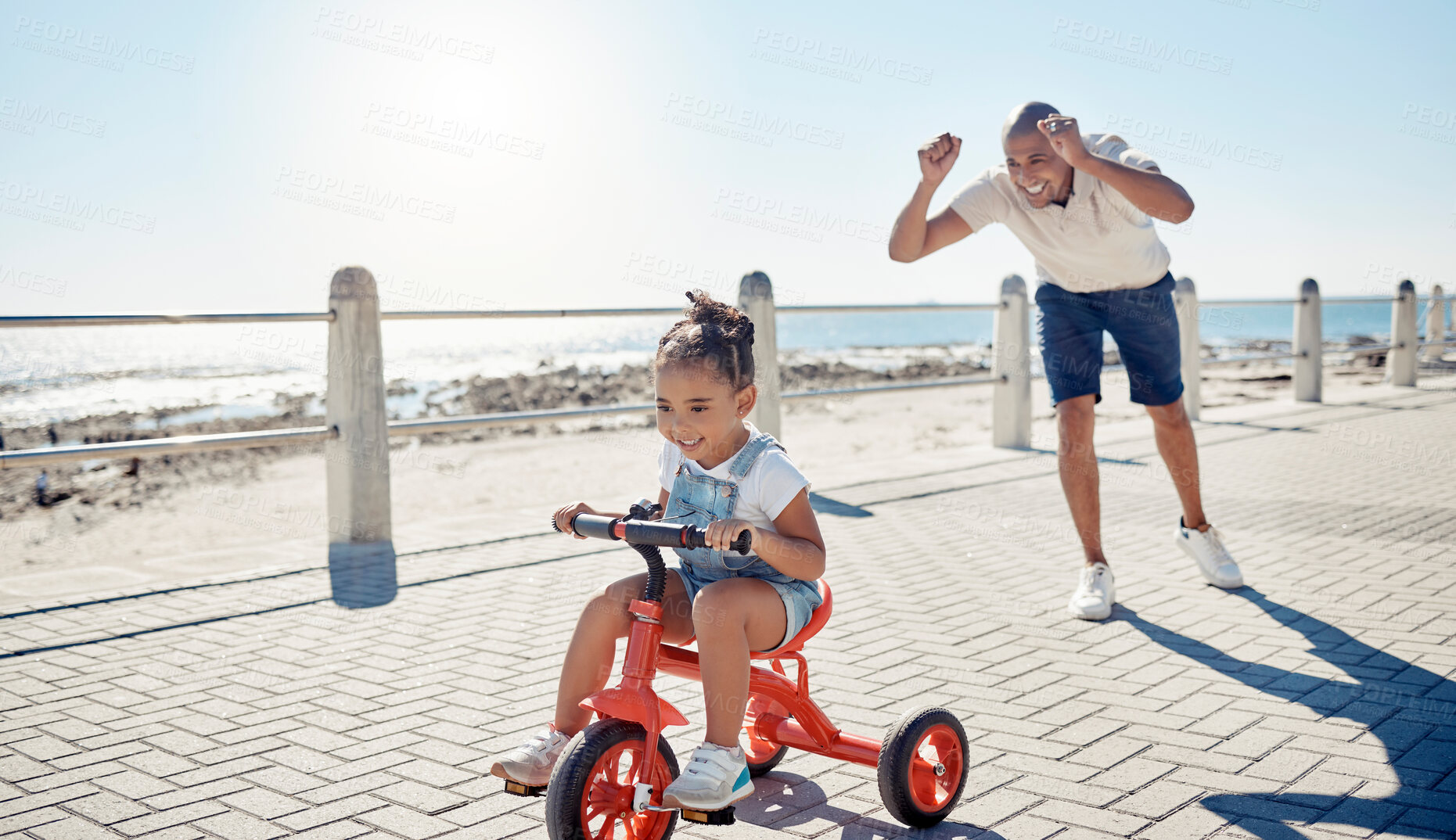 Buy stock photo Ocean, bicycle and happy father with girl excited after learning, teaching and helping kid ride bike. Black family, love and dad celebrate with child on summer holiday, vacation and weekend by sea