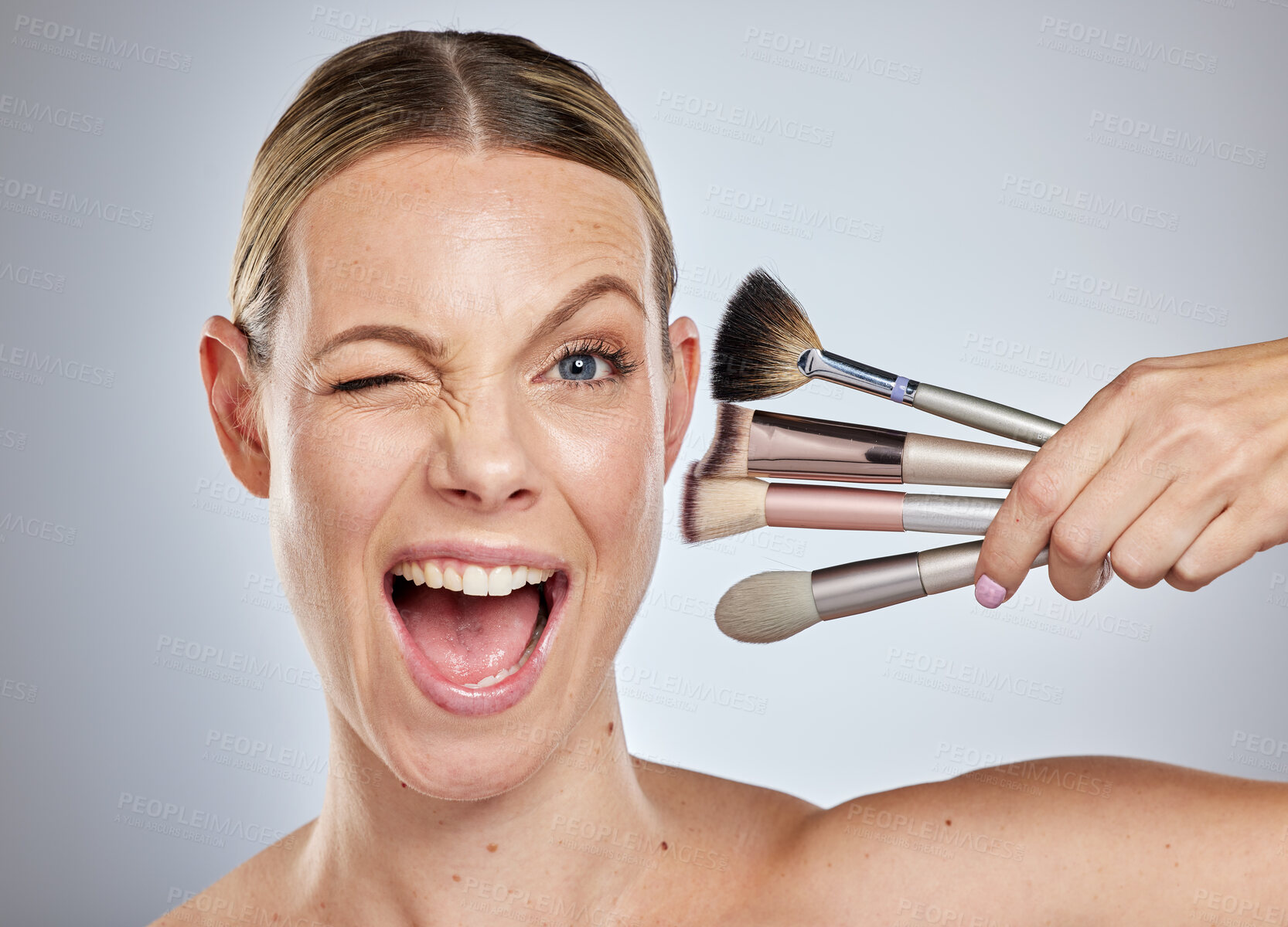 Buy stock photo Woman, face and wink with makeup brushes for cosmetics or facial treatment against a grey studio background. Portrait of female model in beauty holding makeup tools in self care or self love