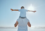 Family, beach and summer vacation for freedom with a child on shoulder of father with hands outstretched for happiness against blue sky. Man and kid son together at sea for trust, nature and peace