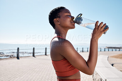 Buy stock photo Black woman, drinking water or bottle in fitness workout, training or exercise by beach, ocean or sea in summer location. Smile, happy or sports runner with drink for healthcare wellness recovery