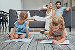 Living room, parents relaxing and children drawing in books on the floor in their modern home. Mother, father and girl kids sitting in the lounge together to rest, draw and bond in their house.