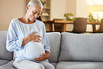 Pregnant black woman, sofa and love for belly in home living room with smile, care and happy. Woman, pregnancy and happiness for future on couch in lounge with vision, thinking and holding stomach