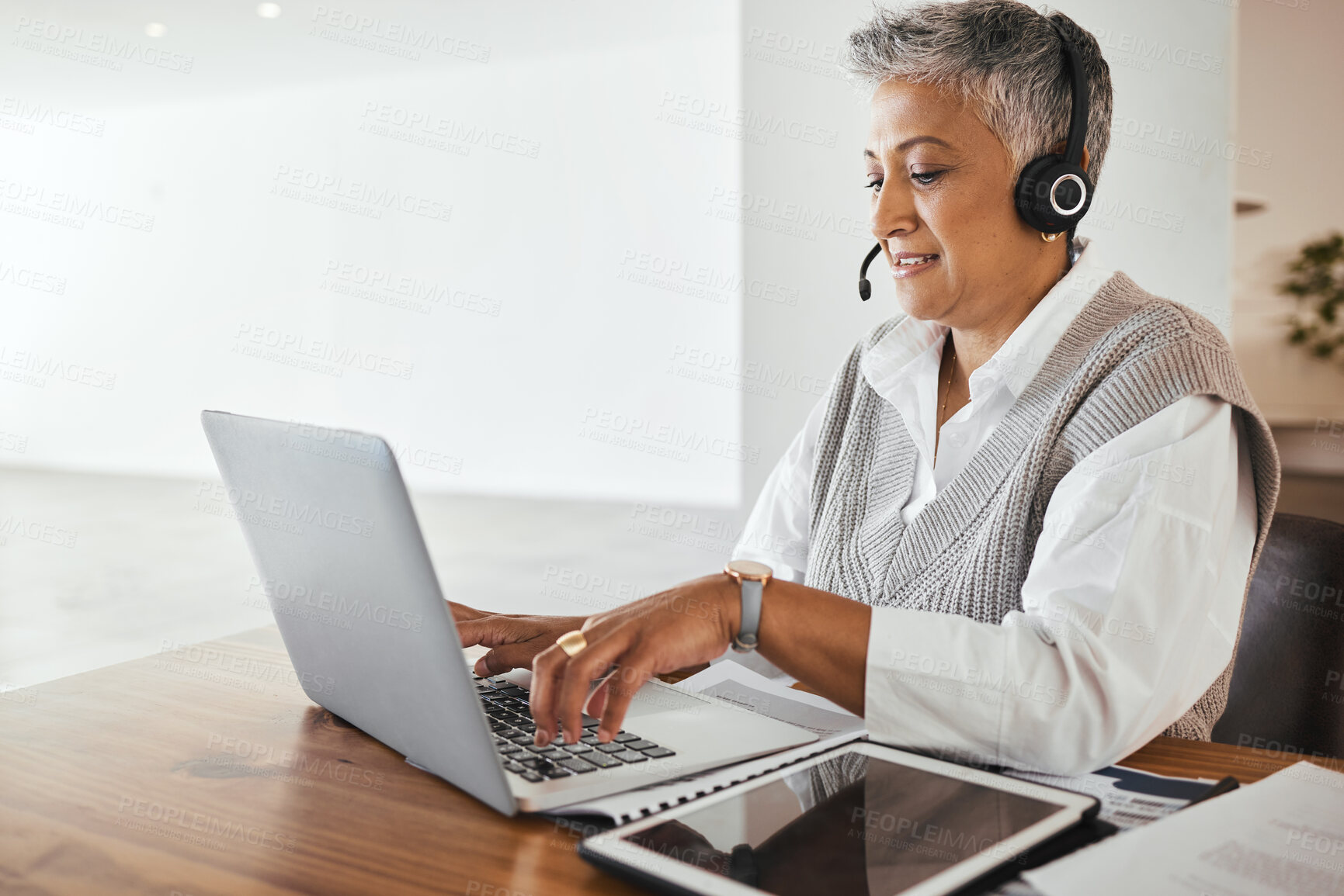 Buy stock photo Call center, receptionist and senior consultant working on a laptop, headset and tablet in the office. Customer support, hotline and elderly female telemarketing agent typing on computer in workplace