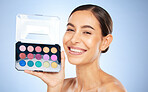 Beauty, makeup and eye shadow pallet with a model woman in studio on a blue background to apply color. Portrait, face and cosmetics with an attractive young female posing to promote a skin product