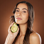 Face portrait, skincare and woman with avocado in studio on a brown background. Beauty, organic cosmetics and young female model with fruit, product or food for healthy diet, nutrition and vitamin c.