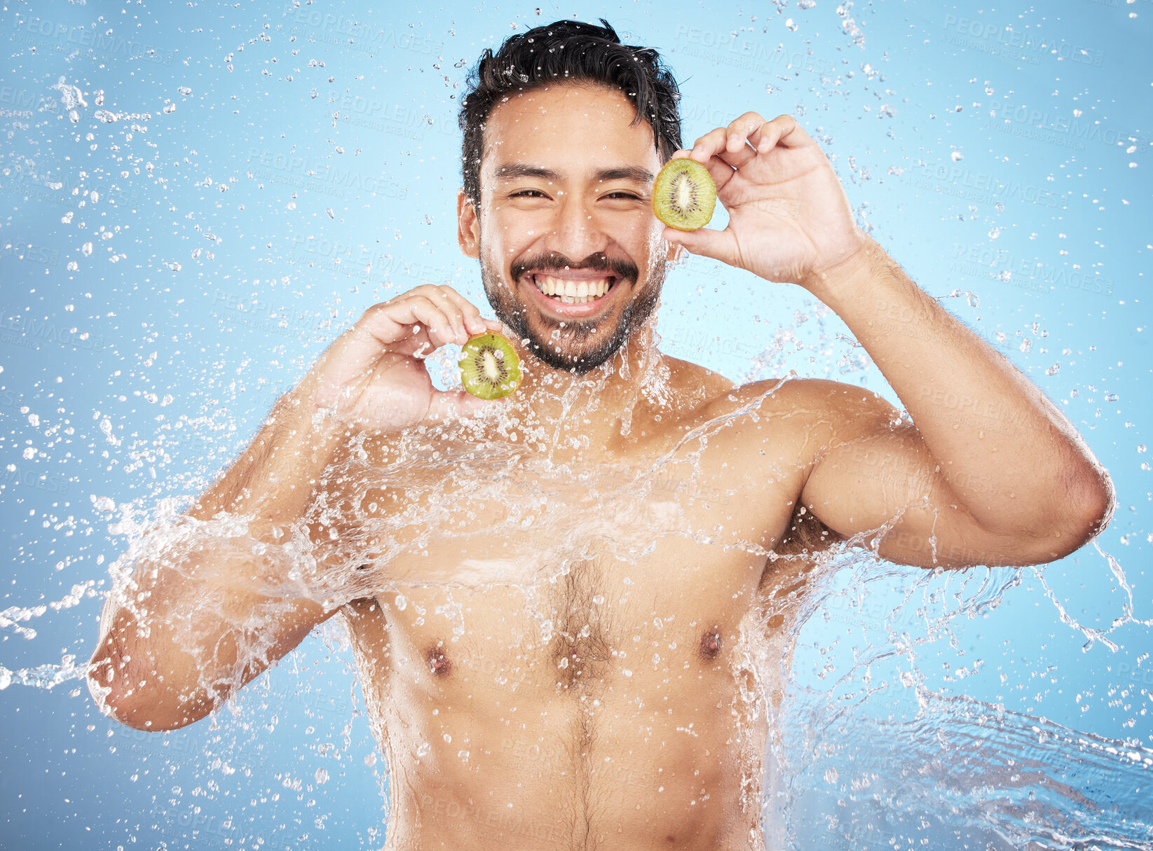 Buy stock photo Face portrait, water splash and man with kiwi in studio isolated on a blue background. Cleaning, skincare and hygiene of happy male model washing fresh fruit for vitamin c, nutrition and healthy diet