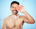 Face, water and grapefruit with a man model in studio on a blue background for hygiene or natural hydration. Skincare, beauty or fruit with a handsome young male wet from a water splash in the shower
