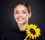 Skincare, beauty and portrait of a woman with a sunflower in a studio for a clean, healthy and organic routine. Cosmetic, floral and model from Brazil with natural face treatment by black background.