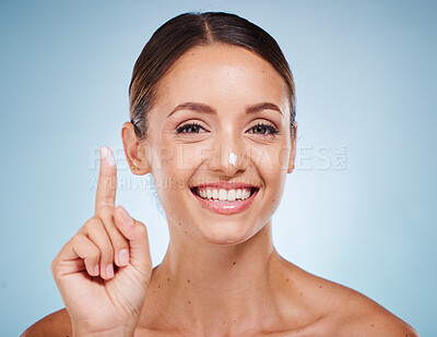 Buy stock photo Portrait, beauty and skincare with a model woman posing in studio on a blue background with lotion on her finger. Face, skin or moisturizer with an attractive young female posing to promote a product