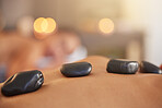 Stone, man or woman at a spa for a massage, relaxing self care or luxury physical therapy healing for back pain. Hot stone massage, zoom or customer on a bed for healthy natural holistic treatment 