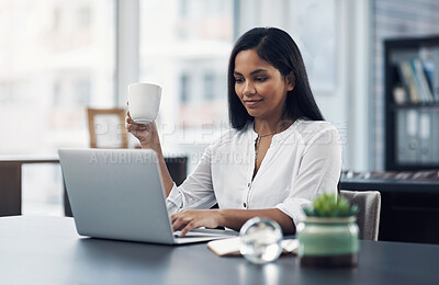 Buy stock photo Shot of a young businesswoman drinking coffee while working on a laptop in an office
