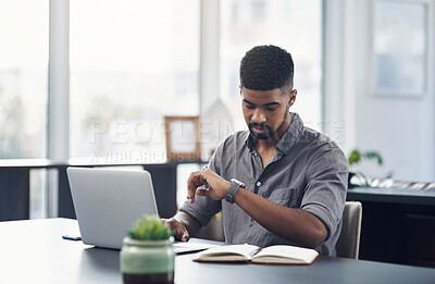 Buy stock photo Shot of a young businessman checking the time while working on a laptop in an office