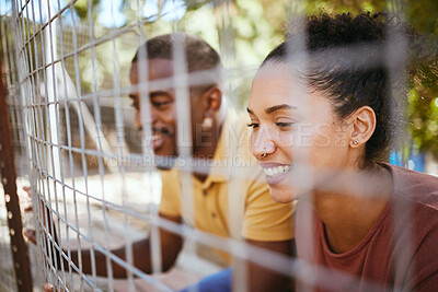 Buy stock photo Happy couple, fence and smile at animal shelter, pet centre or zoo looking for a cute companion to adopt. Black man and woman smiling in happiness behind fencing for adorable fluffy pups for adoption