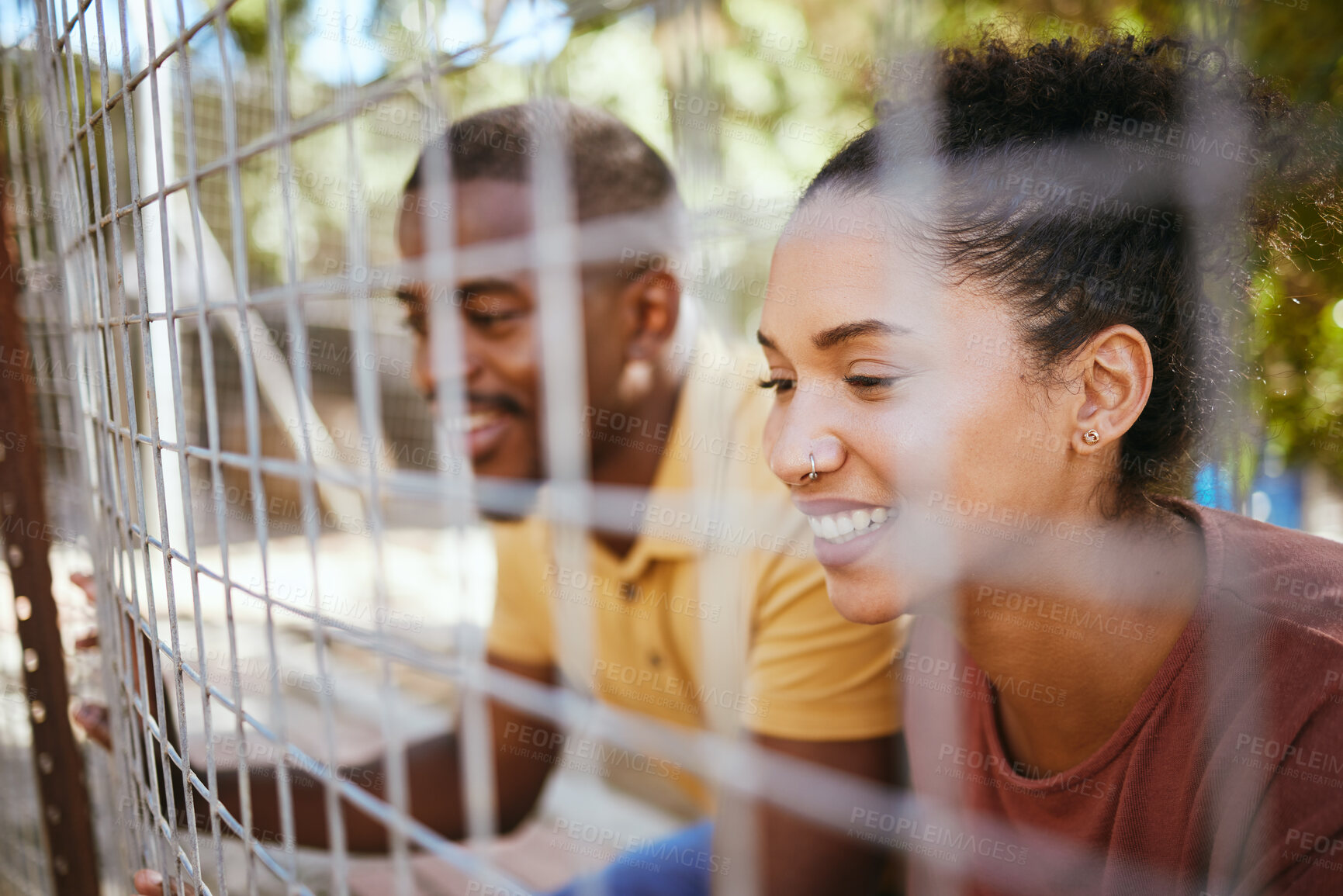 Buy stock photo Happy couple, fence and smile at animal shelter, pet centre or zoo looking for a cute companion to adopt. Black man and woman smiling in happiness behind fencing for adorable fluffy pups for adoption