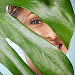 Portrait, skincare and palm leaf with a model woman posing in studio on blue background for beauty. Face, skin or nature with an attractive young female standing behind a plant for natural treatment
