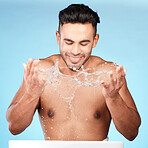 Face, water splash and skincare of man cleaning in studio isolated on a blue background. Hygiene, water drops and male model washing, bathing or grooming for healthy skin, facial wellness or beauty.