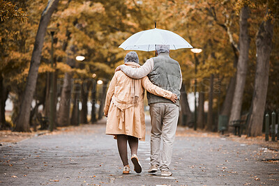 Buy stock photo Elderly, couple walk in park with umbrella and fresh air, outdoor in nature in fall for exercise and retirement together. Hug, love and care with trees, senior man and woman in New York back view.