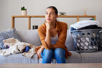 Laundry, bored and break with a woman cleaner sitting on a sofa in her living room at home for spring cleaning. Depression, cleaning and laundry basket with a female housekeeper resting on a couch