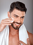 Cosmetics, skincare and man with cotton pad, natural beauty and on grey studio background. Male, guy and makeup with cottonwool, treatment and routine with smile, towel and healthy for luxury and spa