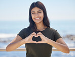 Beach portrait and heart hand woman for summer holiday freedom, happiness and wellness. Happy Indian girl enjoying sun at ocean with love shape and optimistic smile for travel adventure.

