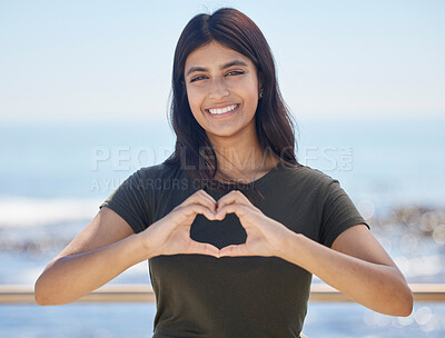 Buy stock photo Beach portrait and heart hand woman for summer holiday freedom, happiness and wellness. Happy Indian girl enjoying sun at ocean with love shape and optimistic smile for travel adventure.

