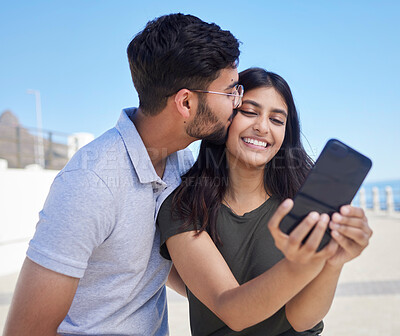 Buy stock photo Phone, selfie and smile with couple at beach, travel and kiss by ocean with support, trust and outdoor for adventure in Mumbai. Smile in picture, happy memory with smartphone photography and romance 