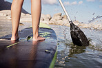 Feet, paddle surf and water with a sports woman standing on a paddle board in the sea, ocean or a river outdoor. Back, balance and sport with a female athlete outside for fitness, exercise or hobby