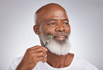 Buy stock photo Senior black man, skincare and facial roller to massage skin during self care for wellness, dermatology and cosmetics. Headshot of male with beauty tool on grey studio background for a spa treatment