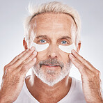 Senior man with collagen eyes mask in skincare, dermatology facial and face cosmetics advertising in studio portrait. Elderly model with hands application of eye patch, anti aging product and beauty
