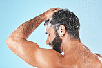 Face, shampoo shower and water splash of man in studio isolated on a blue background. Water drops, hair care and back of male model washing, cleaning or bathing for healthy skin, skincare and hygiene