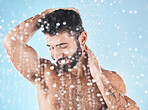 Water splash, face and man in shower for skincare in studio isolated on a blue background. Water drops, dermatology and male model cleaning, washing or bathing for wellness, healthy skin and hygiene.