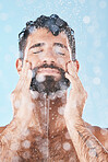 Face, skincare shower and water splash of man in studio isolated on a blue background. Water drops, dermatology and male model washing, cleaning or bathing for healthy skin, wellness and hygiene.