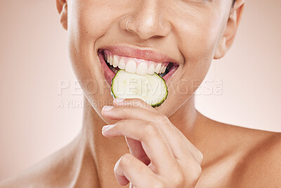 Buy stock photo Hand, mouth and cucumber with a model black woman biting a vegetable in studio on a beige background. Health, beauty and skincare with a young female eating a slice of veg for natural wellness