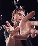 Man, hands and bubbles in studio for magic, art performance or creative show by black background. Model, artist and soap with rainbow light, dark mystery aesthetic or theater presentation by backdrop