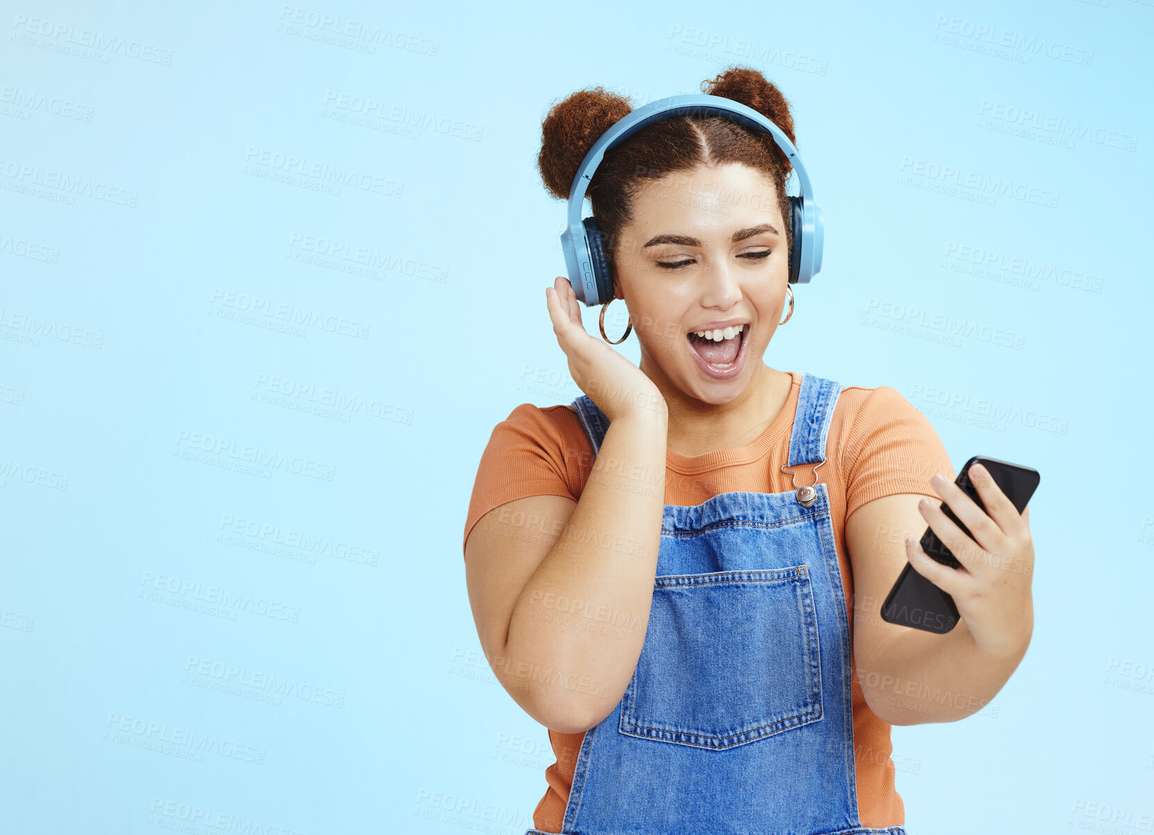 Buy stock photo Mockup, smartphone and woman with headphones, excited and smile on blue studio background. Happy, female or girl with cellphone, headset or steaming music, social media or podcast to relax or listen 