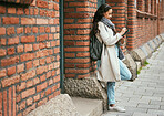 Woman, student and tablet relaxing on brick wall writing, design or doing research in the city. Female university learner or designer working on touchscreen with wireless pen or tech in a urban town