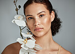 Skincare, face portrait and woman with orchid in studio isolated on a gray background. Floral makeup, organic cosmetics and female model with flowers for healthy skin treatment, wellness and beauty.