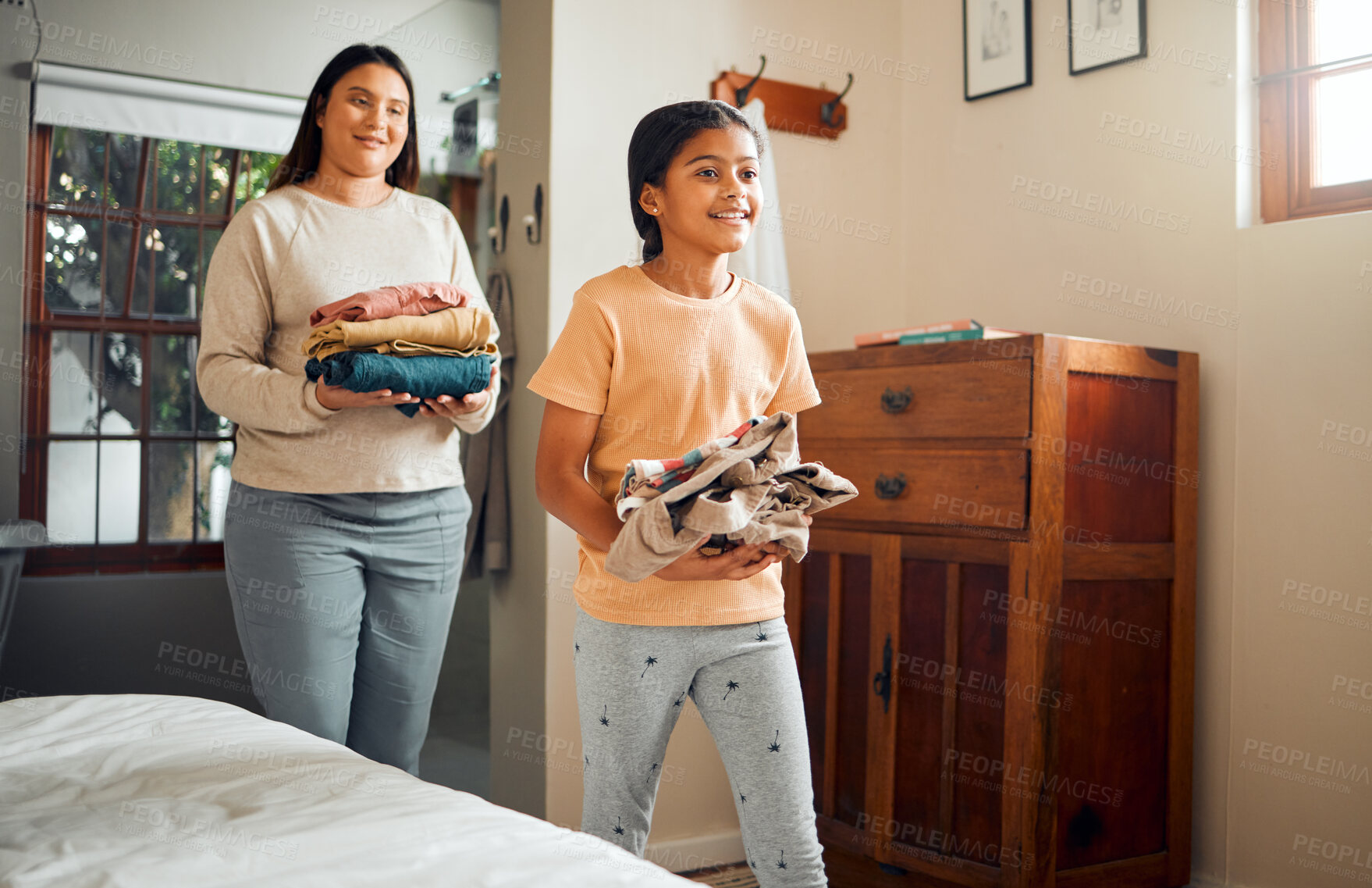 Buy stock photo Little girl, mom and helping with laundry for chores, clothing or folded washing with smile at home. Happy child walking with mother carrying clean clothes for hygiene, housework or routine indoors