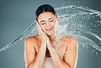 Water, splash and beauty with a woman in studio on a blue background for hygiene or hydration in the shower. Spa, wellness and cleaning with an attractive young female washing in the bathroom