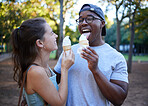 Interracial, ice cream or couple of friends in a park walking on a fun romantic date in nature bonding together. Romance, relaxed black man and happy woman loves eating a snack on a holiday vacation