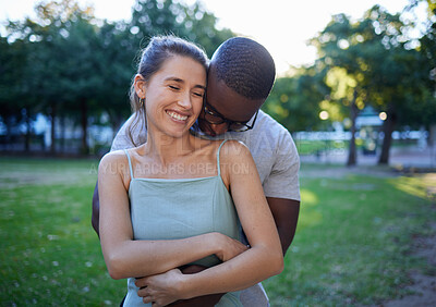 Buy stock photo Happy interracial couple, hug and smile for romance, love or care or together in a nature park. Woman smiling with man hugging her for relationship embrace, support or trust kissing shoulder outside