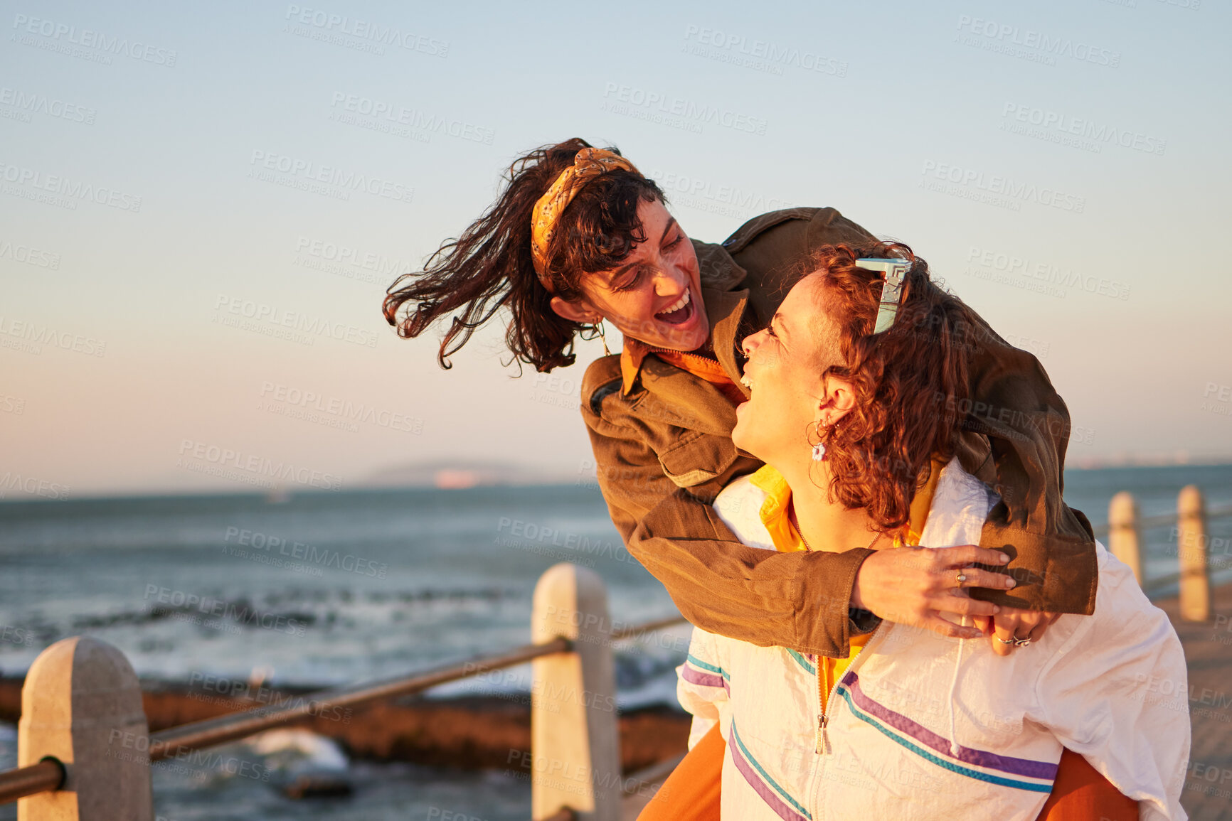 Buy stock photo Women, gay couple and piggyback by the ocean coast with smile for happy relationship and fun pride in the outdoors. Lesbian woman on back ride with partner laughing in joy and happiness by the beach