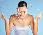 Water splash, skincare and woman isolated on blue background for beauty, cosmetics cleaning and happy. Smile of person or model washing face for dermatology, facial wellness and aesthetic in studio