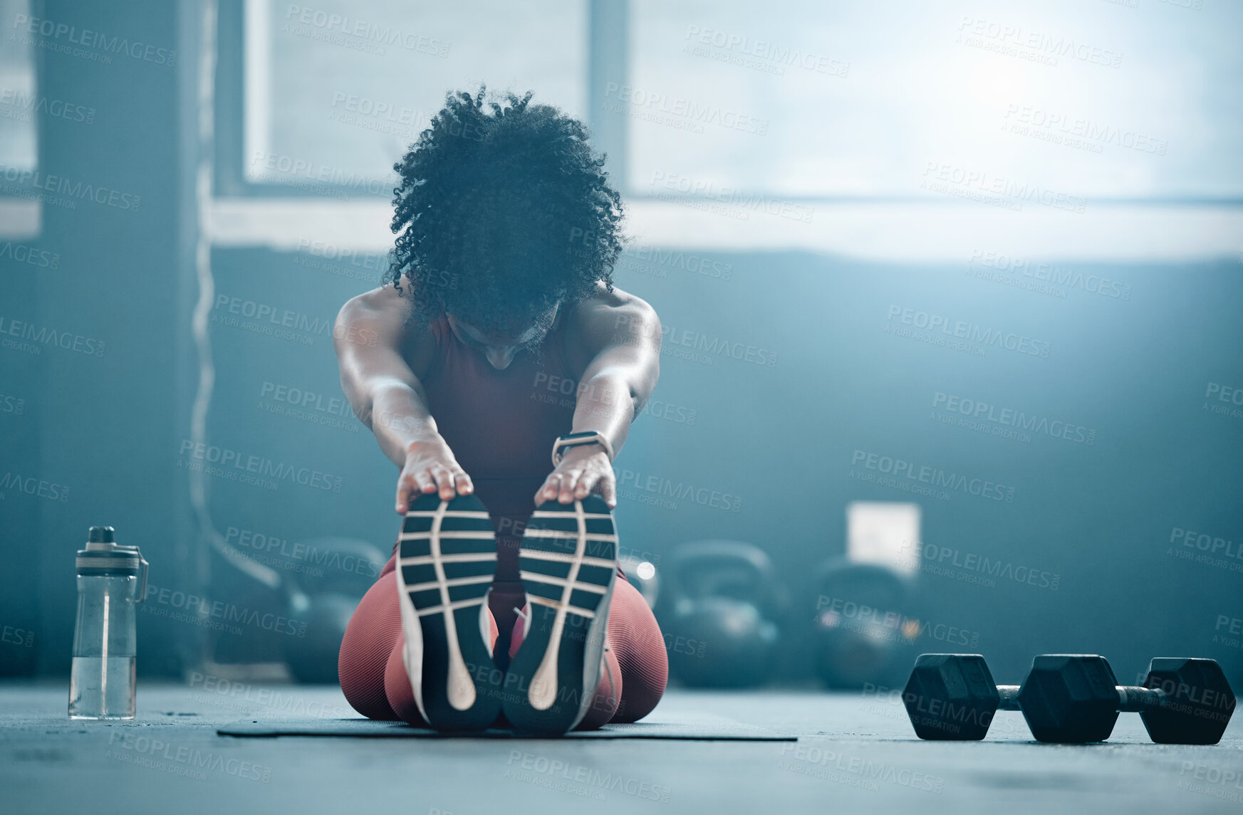 Buy stock photo Fitness, mockup and a black woman stretching in the gym with dumbbells while holding her feet. Health, exercise and weightlifting with a female athlete doing her warm up routine in a workout center